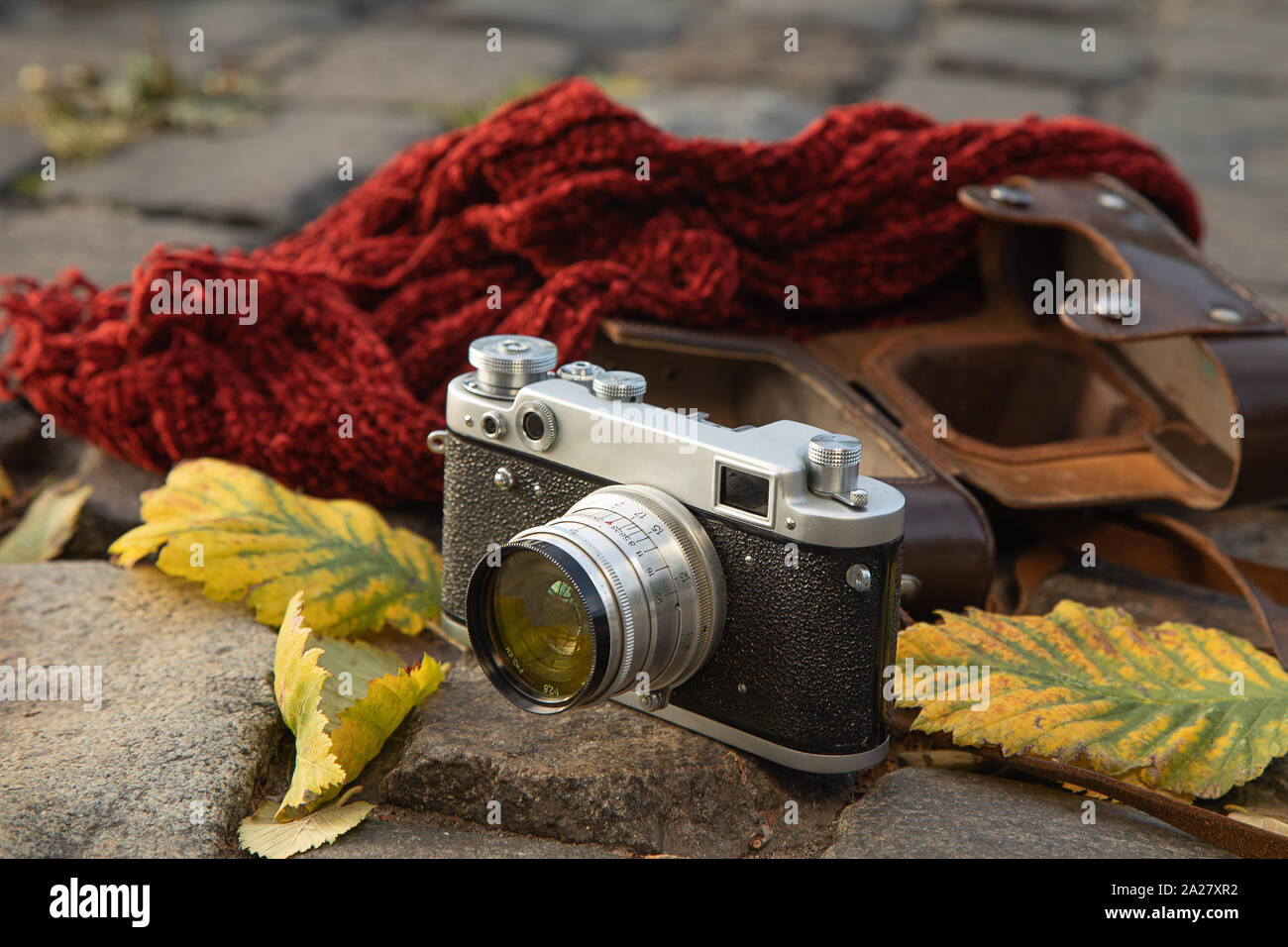 Herbstliche Stimmung noch Leben: vintage Kamera, braunem Leder Holster, roter Schal und Blätter zur Festlegung auf Pflaster Stockfoto