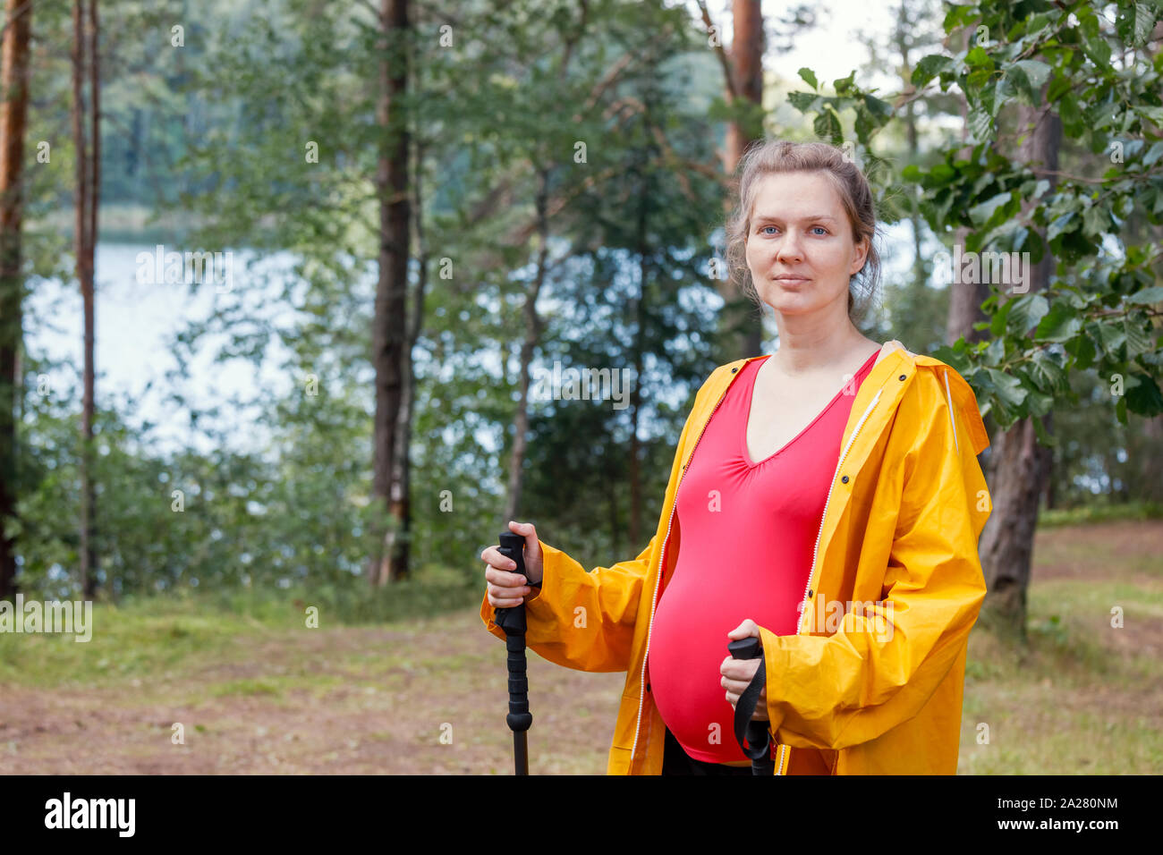 Portrait von jungen schwangeren Frau mit regenmantel im Sommer Wald holding Wanderstöcke Natur genießen - gesunde Schwangerschaft lifestyle Konzept Stockfoto