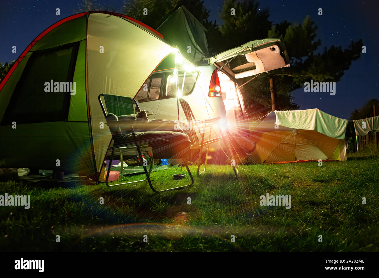 Camping in der Nacht, Zelt mit Stühlen und ein Auto im Hintergrund. Campering unter Sternenhimmel. Stockfoto