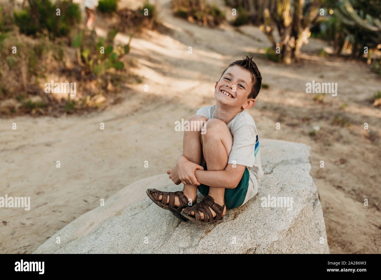 Portrait von älteren Junge sitzt auf Felsen und lächelnd in Cactus Garden Stockfoto