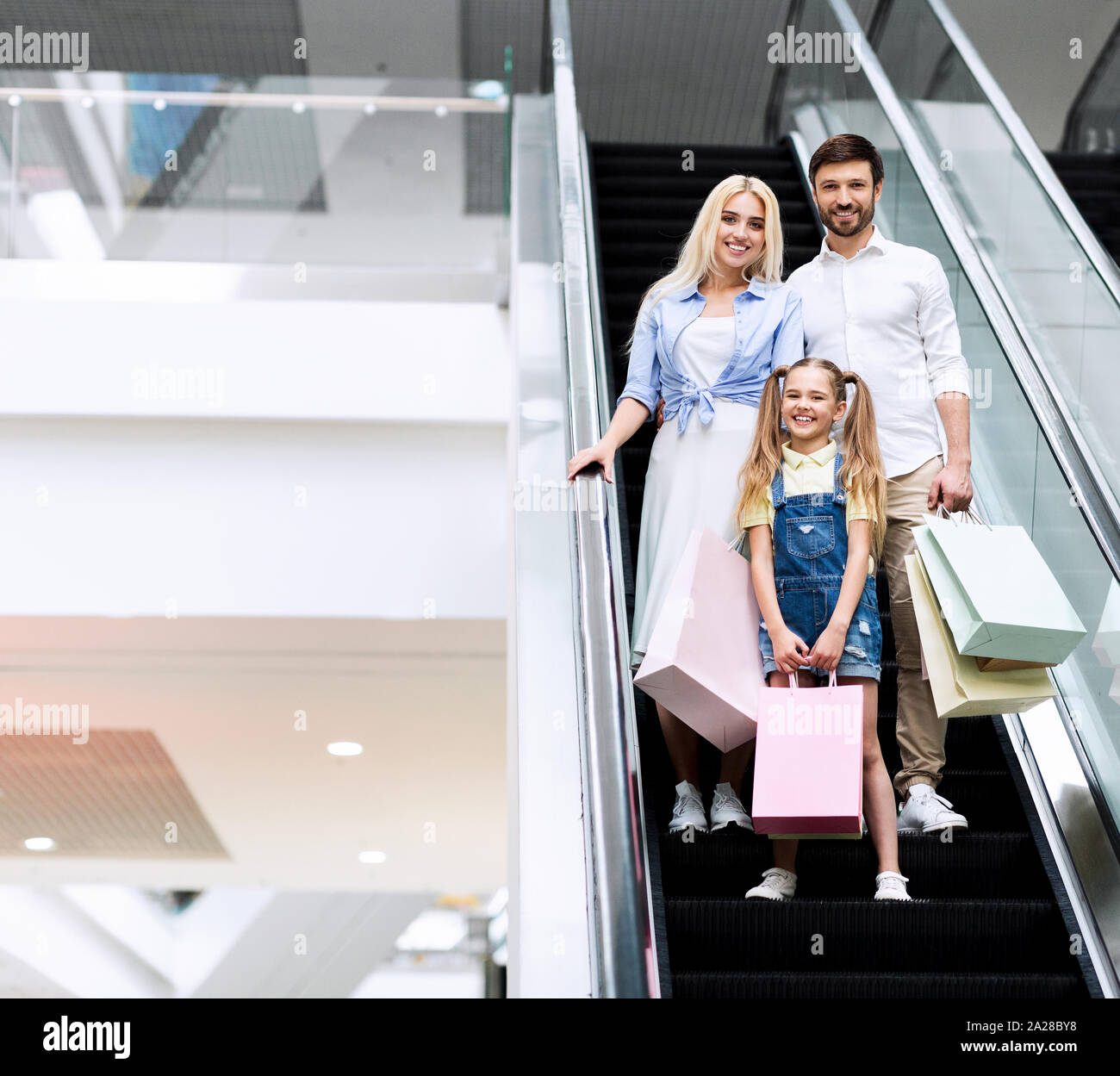 Junge Eltern und Tochter stehen auf Rolltreppe in Shopping Mall Stockfoto