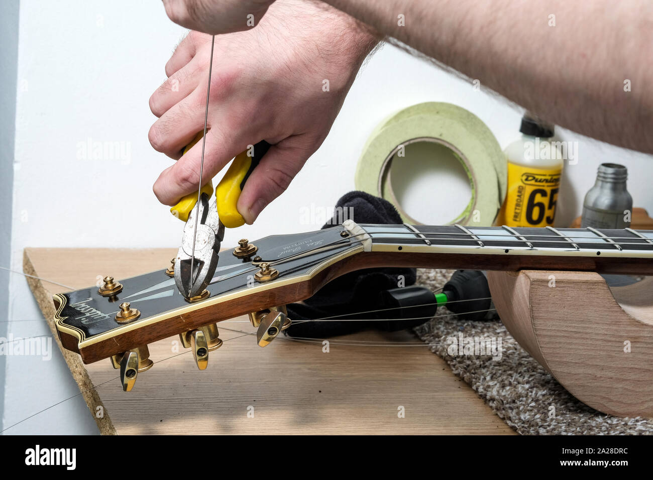 Eine Gitarre Techniker oder Tech, re Aneinanderreihung eine Gibson Gitarre in seiner Werkstatt. Die neue Saiten werden nach um ein Tuning post Wunde geschnitten Stockfoto