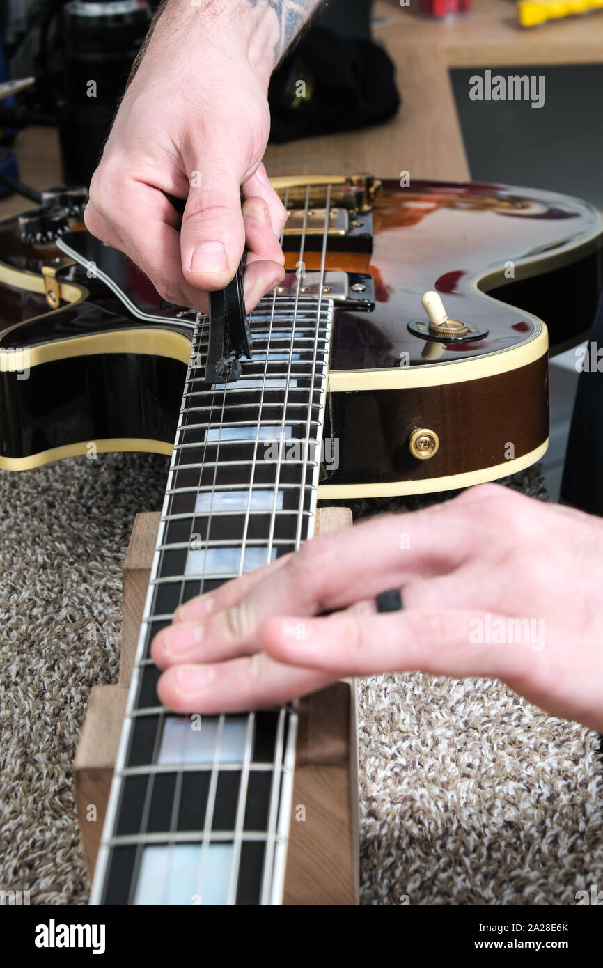 Eine Gitarre Techniker oder Tech, re Aneinanderreihung eine Gibson Gitarre in seiner Werkstatt. Die neue Saiten werden nach der Gitarre angebracht werden gestreckt Stockfoto