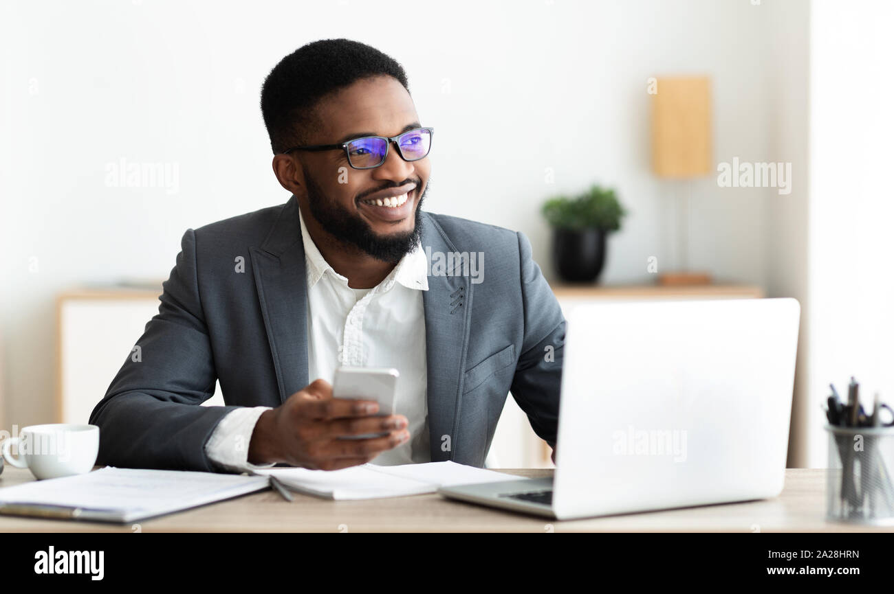 Portrait von lächelnden schwarzer Geschäftsmann am Arbeitsplatz sitzend mit Handy Stockfoto