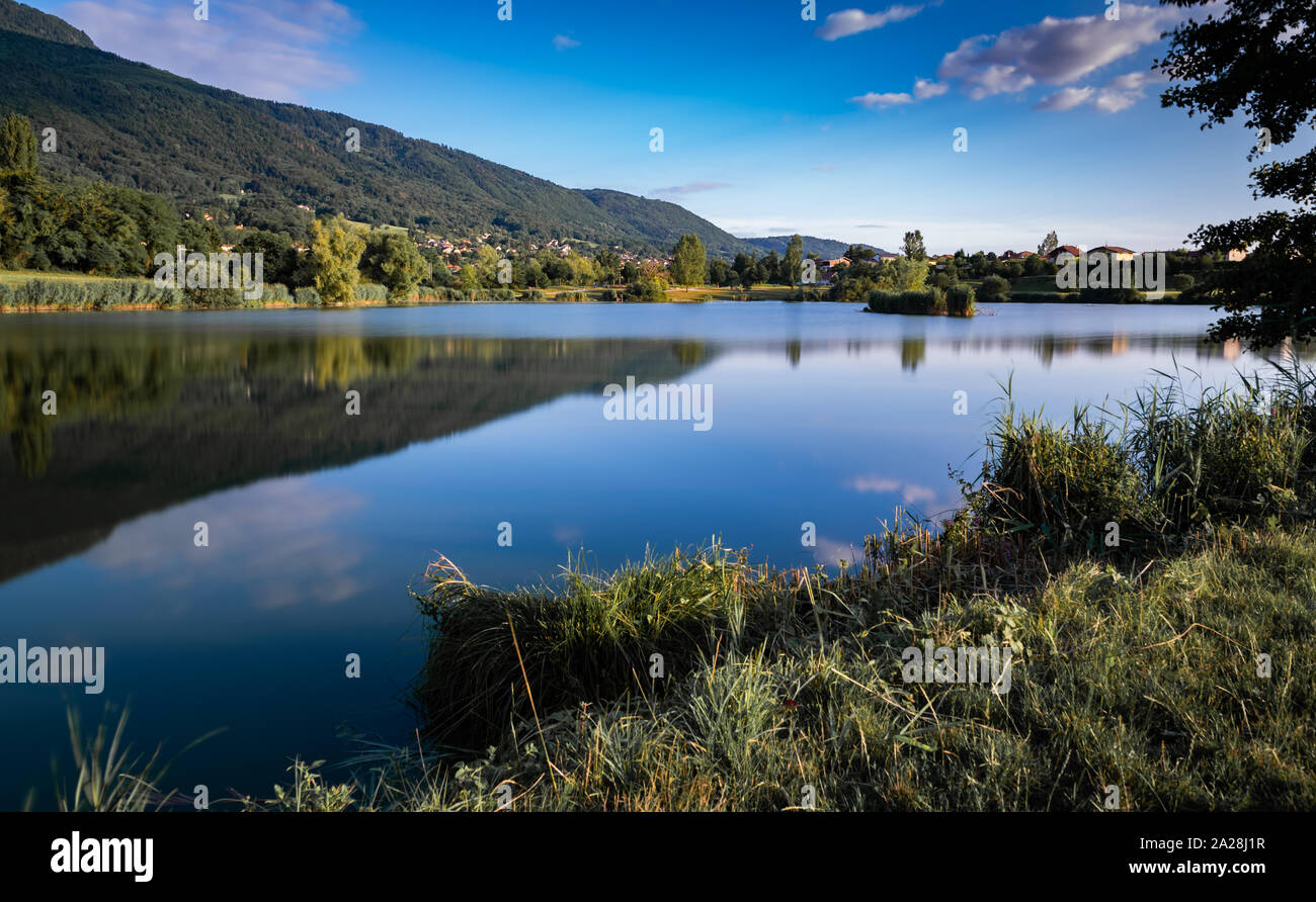Landschaft, der See, die Berge, Vegetation, Dorf und blauer Himmel mit weißen Wolken. Foto mit grau Filter und langen Belichtungszeit. See Machilly. Stockfoto