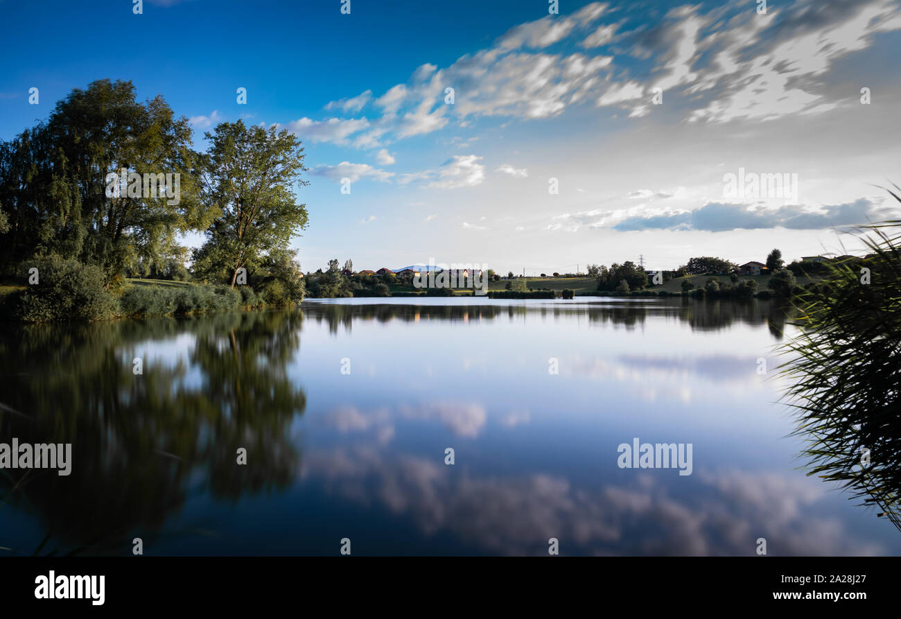 Landschaft, der See, die Berge, Vegetation, Dorf und blauer Himmel mit weißen Wolken. Foto mit grau Filter und langen Belichtungszeit. See Machilly. Stockfoto