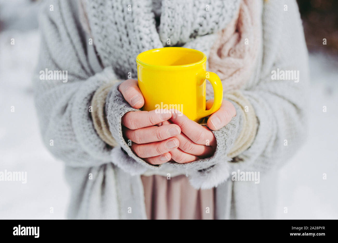 Boho Mädchen, die einen weichen, gewebten Pullover tragen, ist im Winter draußen und hält eine gelbe Tasse warmen Getränks in den Händen. Geringe Schärfentiefe. Stockfoto