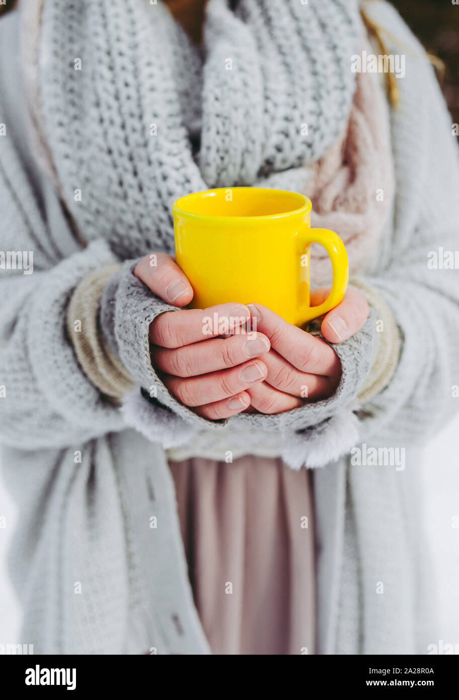 Boho Mädchen, die einen weichen, gewebten Pullover tragen, ist im Winter draußen und hält eine gelbe Tasse warmen Getränks in den Händen. Geringe Schärfentiefe. Stockfoto