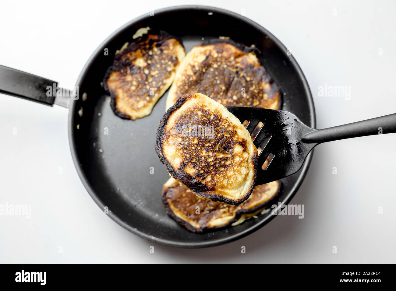 Kochen ist fehlgeschlagen, verbrannte Pfannkuchen auf einer schwarzen Pan, ein Pfannkuchen auf einer Spachtel. Stockfoto