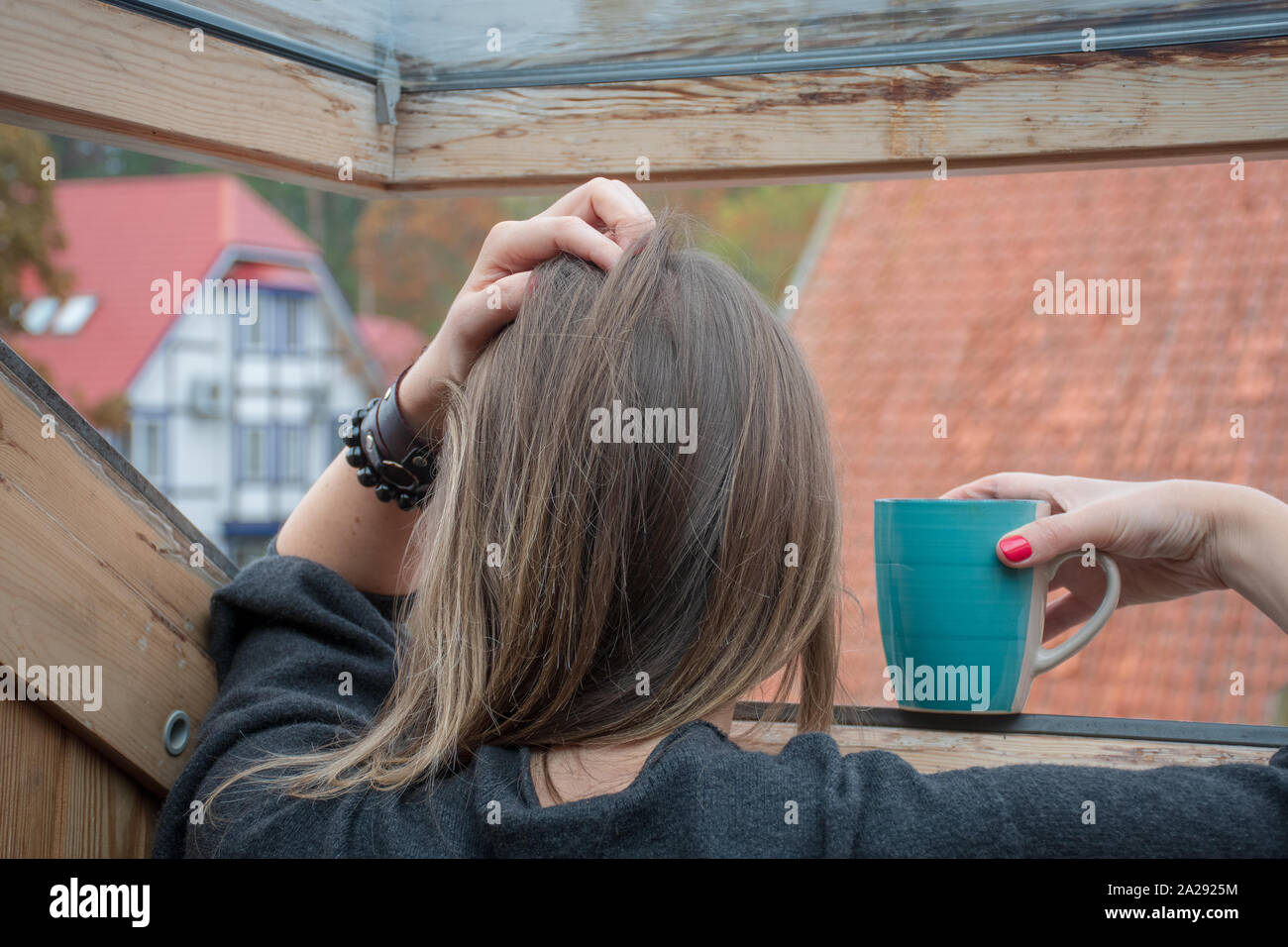 Frau oder ein Mädchen mit einem Becher Blick durch das Fenster in einem verregneten Tag mit einer Hand auf den Kopf Stockfoto