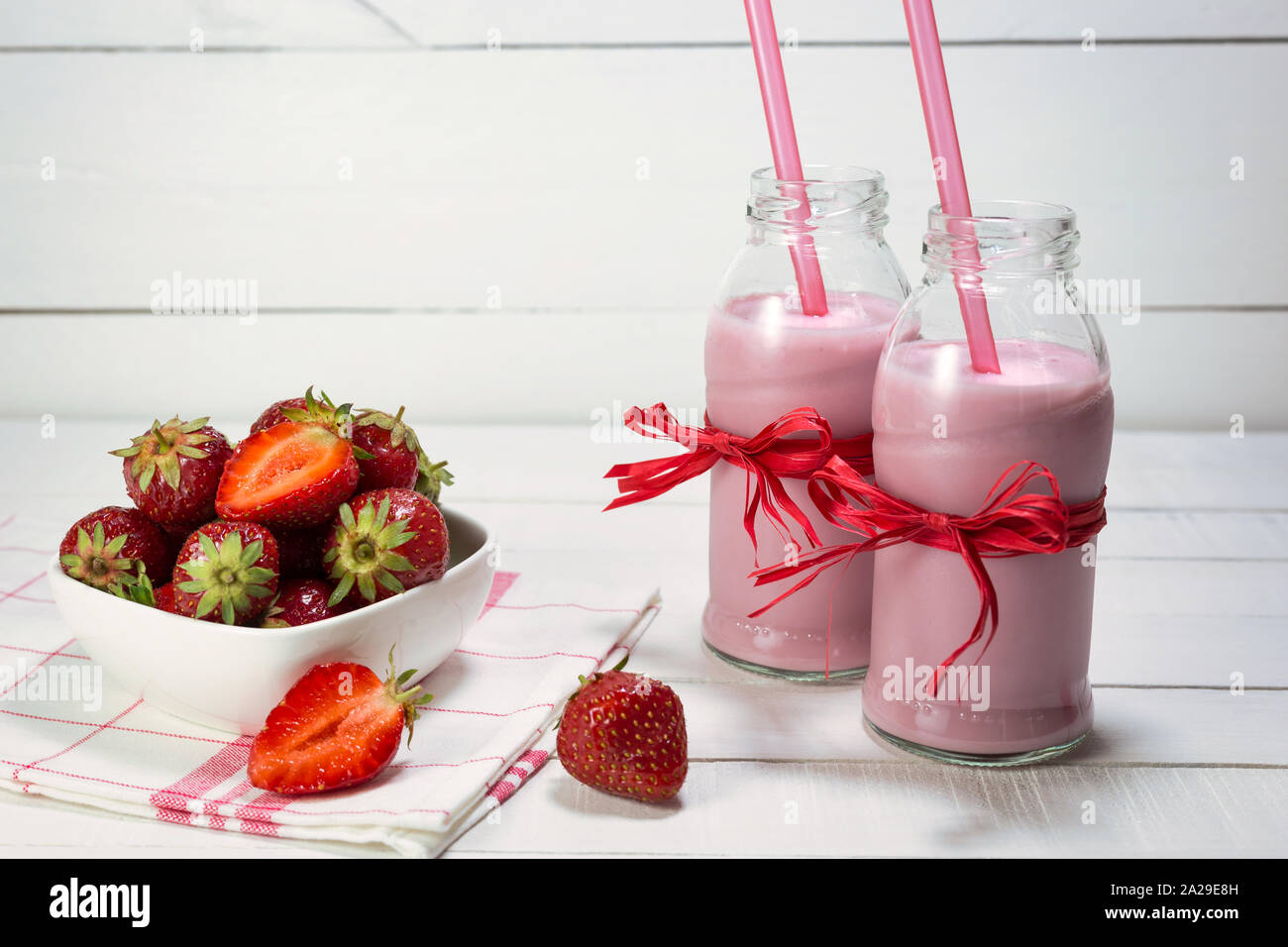 Erdbeer Joghurt in Flaschen und frische Erdbeeren auf einem weißen Holztisch. Gesunde Ernährung Konzept. Stockfoto