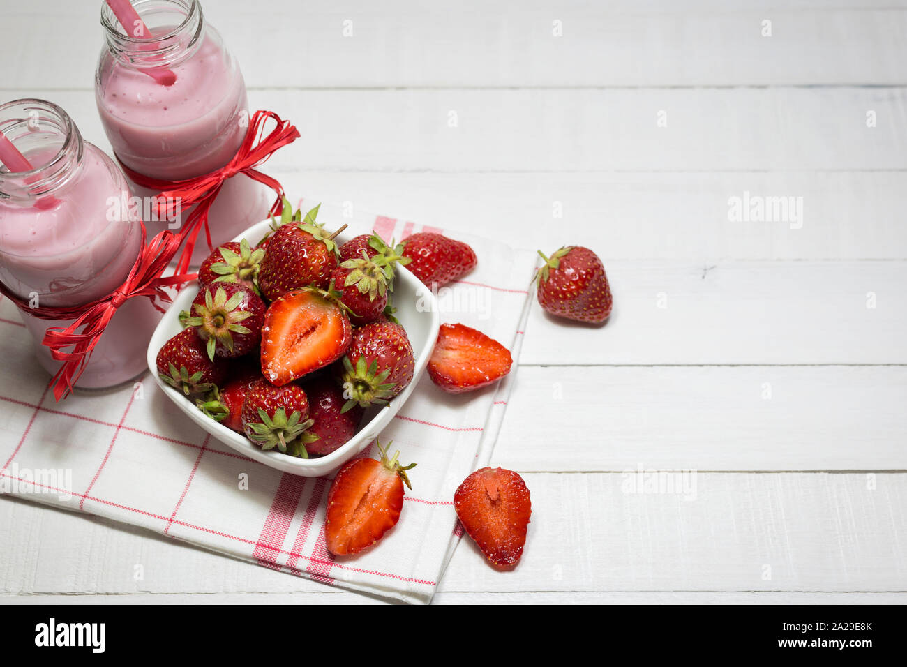 Erdbeer Joghurt in Flaschen und frische Erdbeeren auf einem weißen Holztisch. Gesunde Ernährung Konzept. Stockfoto