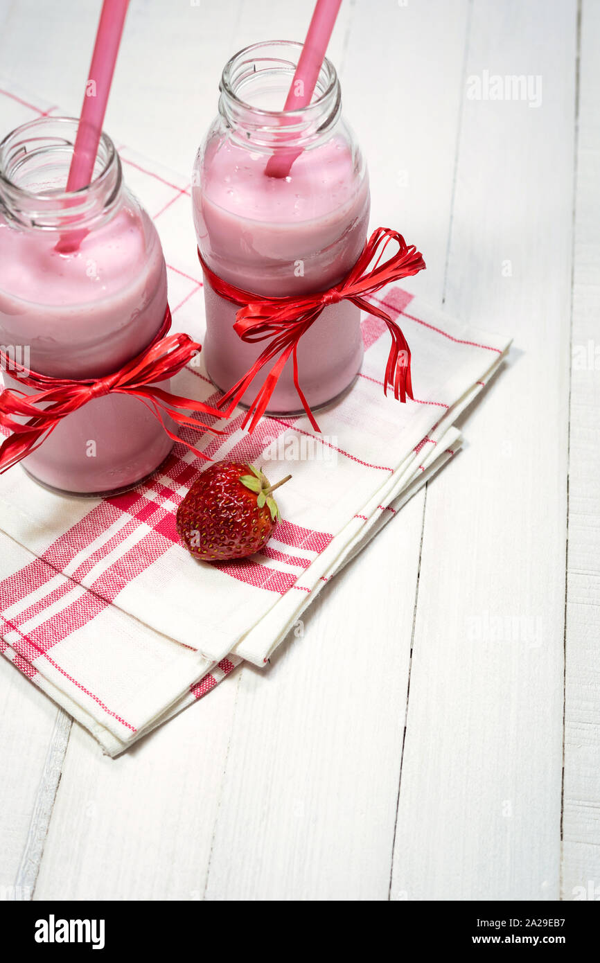 Erdbeer Joghurt in Flaschen und frische organische Erdbeere auf einem weißen Holztisch. Gesunde Ernährung Konzept. Stockfoto