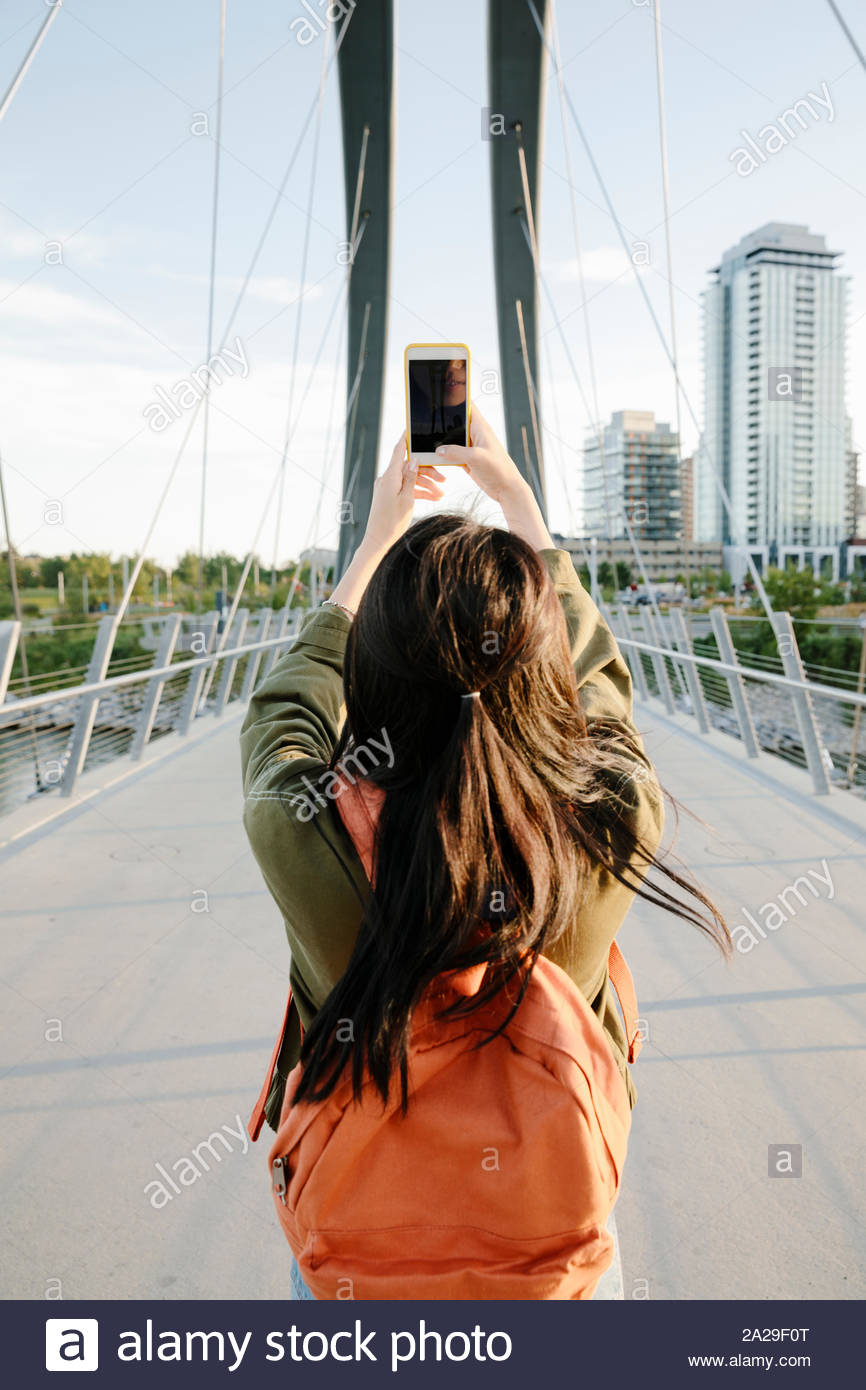 Junge Frau mit Rucksack mit Fotohandy auf städtischen Brücke Stockfoto