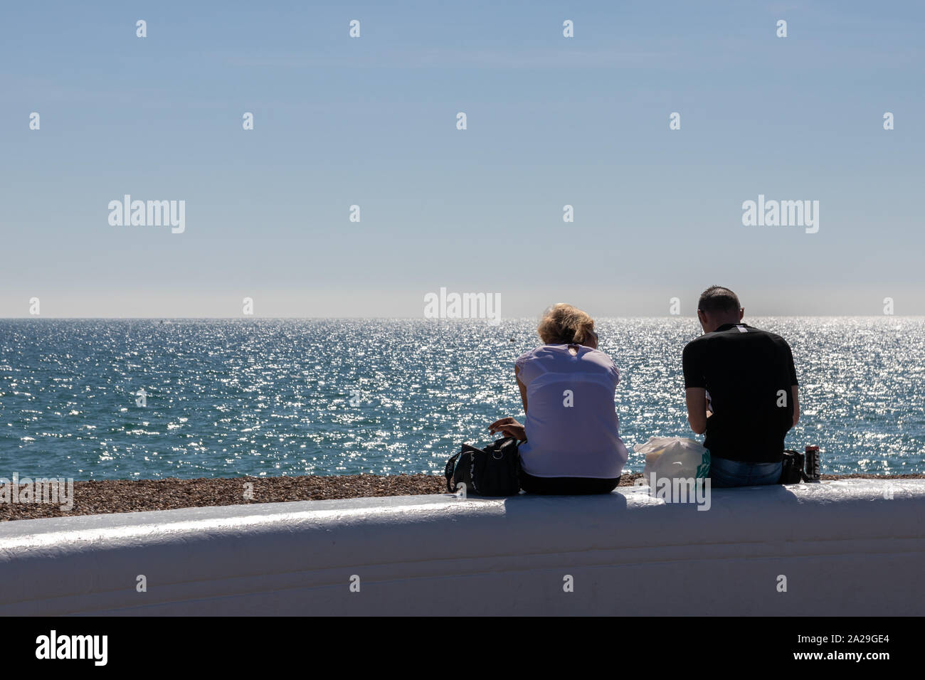 Ein Paar an einer Wand am Meer an einem Sommertag sitzend genießen den Blick auf das Meer Stockfoto