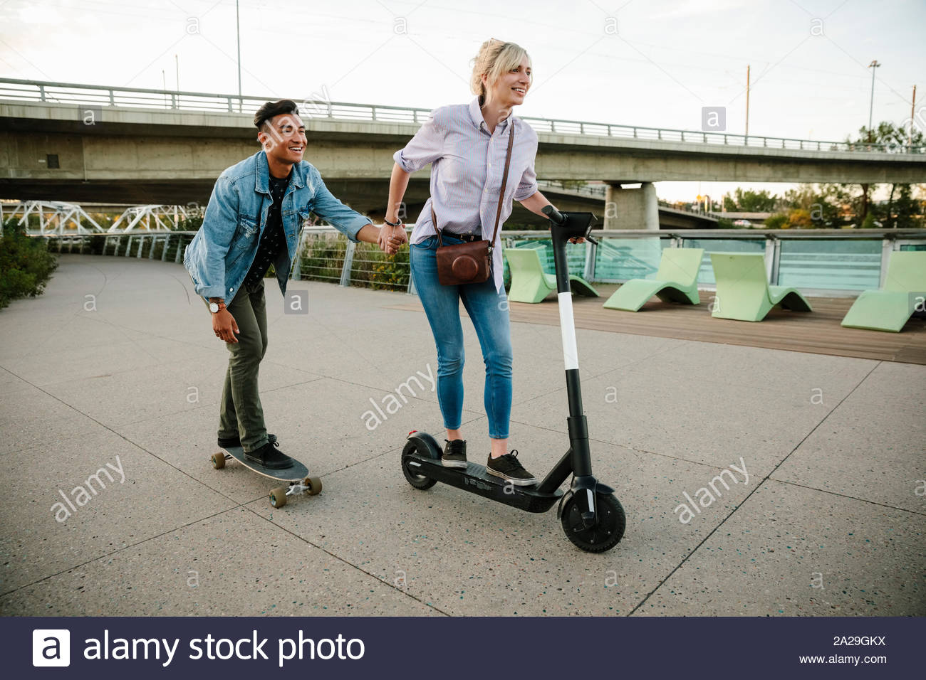 Verspielte junge Paar reiten Roller und Skateboard auf städtischen Bürgersteig Stockfoto