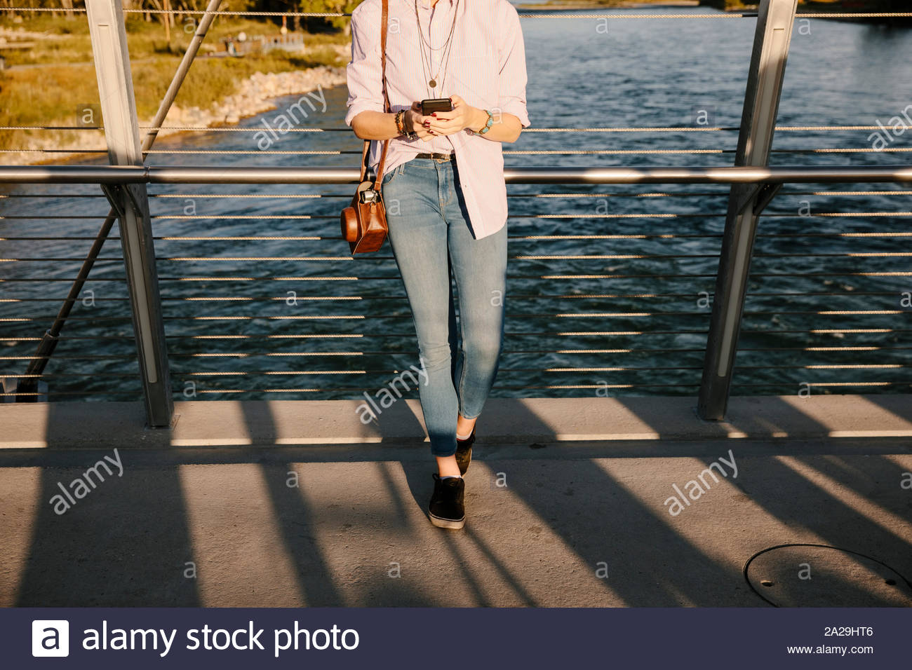 Junge Frau mit Smart Phone auf Brücke über sonnige Fluss Stockfoto