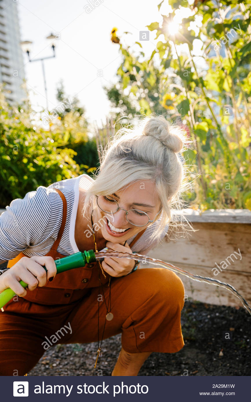 Glückliche junge Frau trinkt aus dem Schlauch im sonnigen Garten Stockfoto