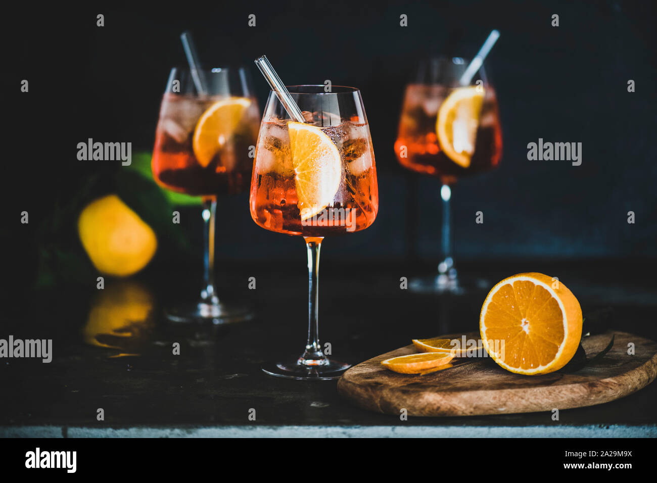 Aperol Spritz Aperitif mit Orangen und Eis im Glas mit umweltfreundlichen Glas Stroh auf konkrete Tabelle, schwarzer Hintergrund, selektiven Fokus. Sommer refres Stockfoto