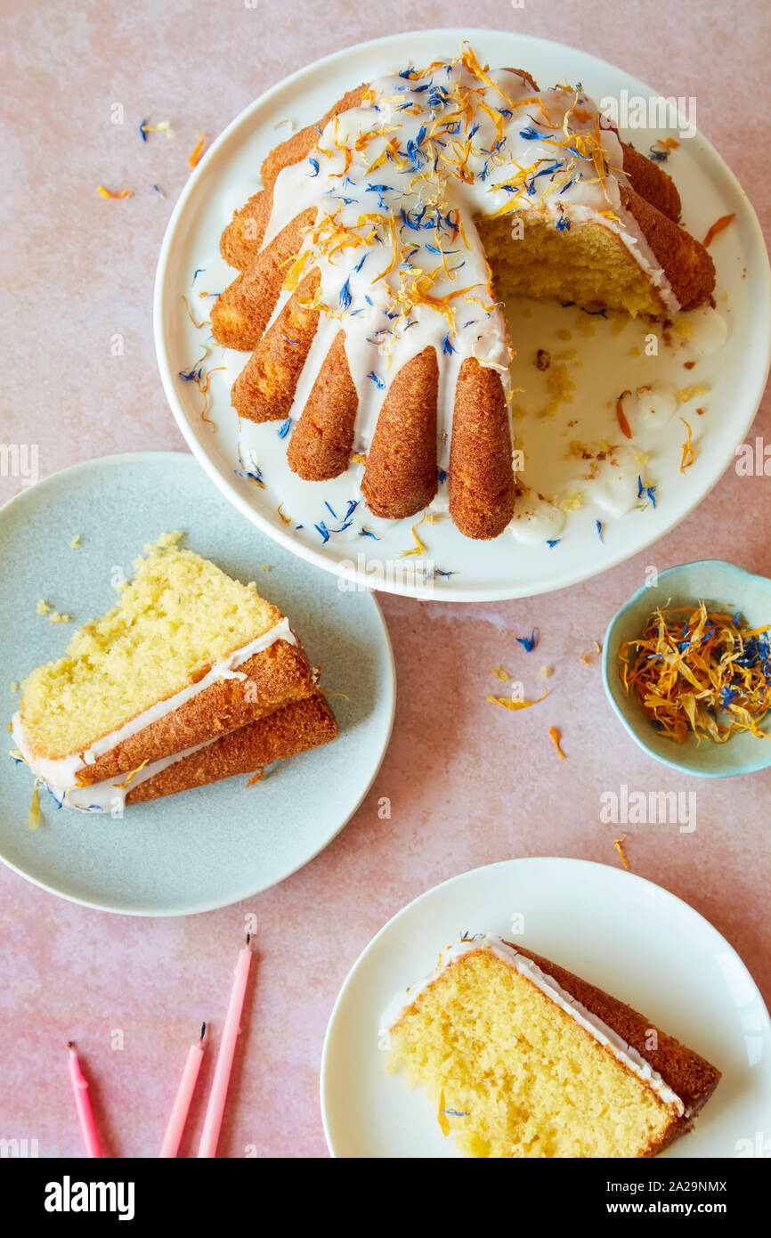 Lemon Drizzle Geburtstag Kuchen mit Puderzucker und essbaren Blüten Stockfoto