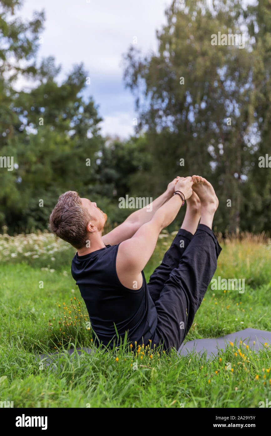 Man Yoga Asanas im City Park inspiriert. Fitness im Freien und Life Balance Konzept. Boot Pose oder Navasana. Stockfoto