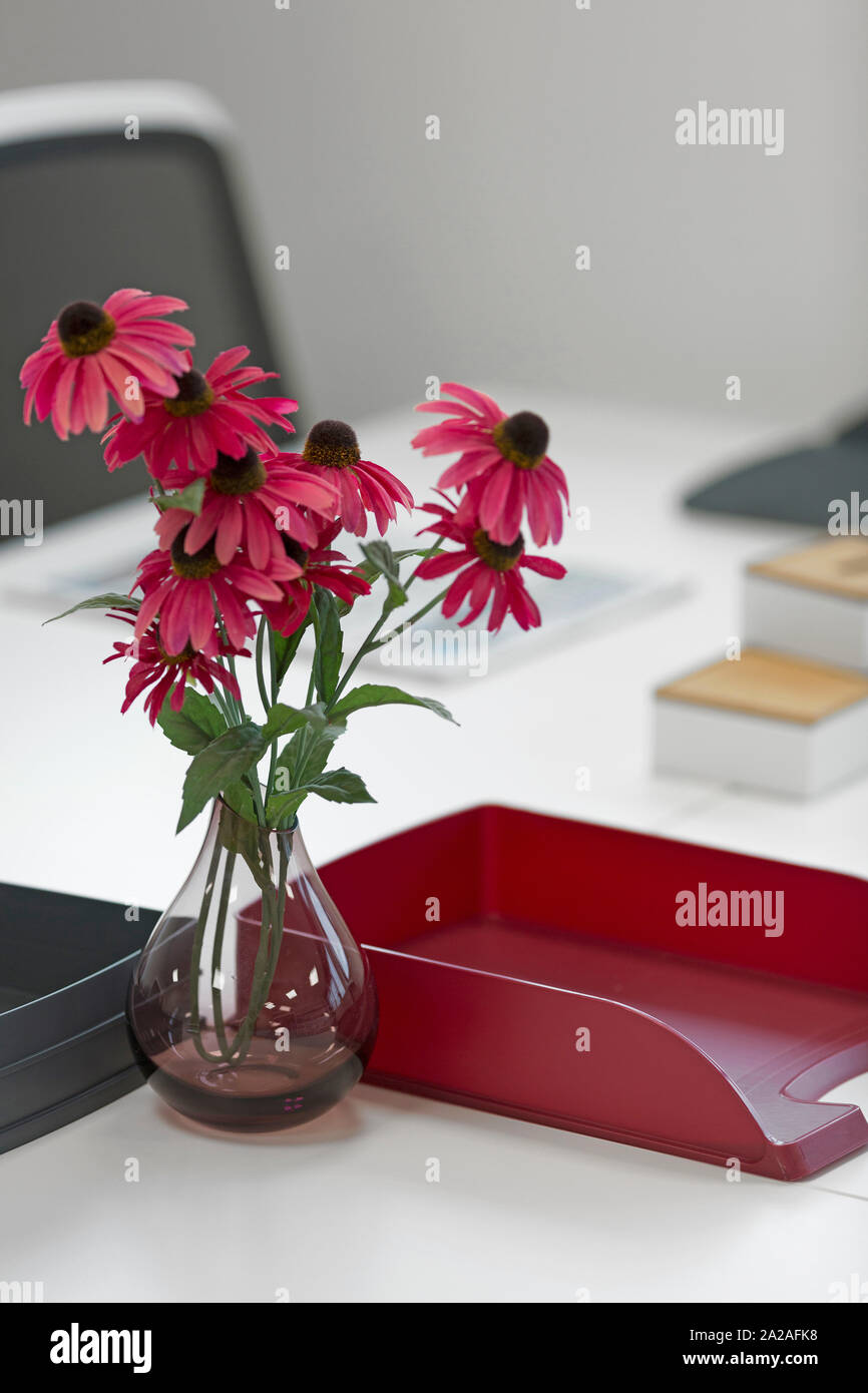 Moderne Büro Schreibtisch mit leuchtend roten Blüten und die Ablage Tabletts Stockfoto