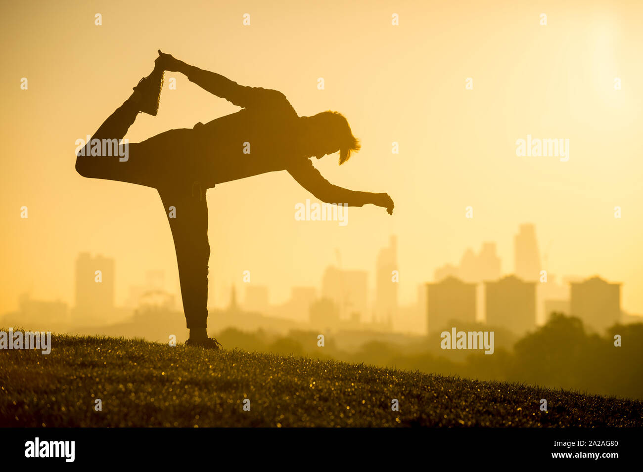 Golden sunrise Blick auf die Silhouette eines Mannes Stretching vor der Skyline der Stadt auf einem Hügel in London, Großbritannien Stockfoto