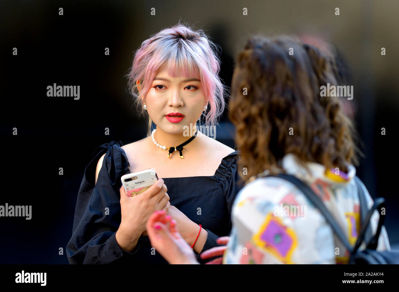 Junge japanische Frau mit Mobiltelefon und rosa Haare an der London Fashion Week, 2019. Stockfoto