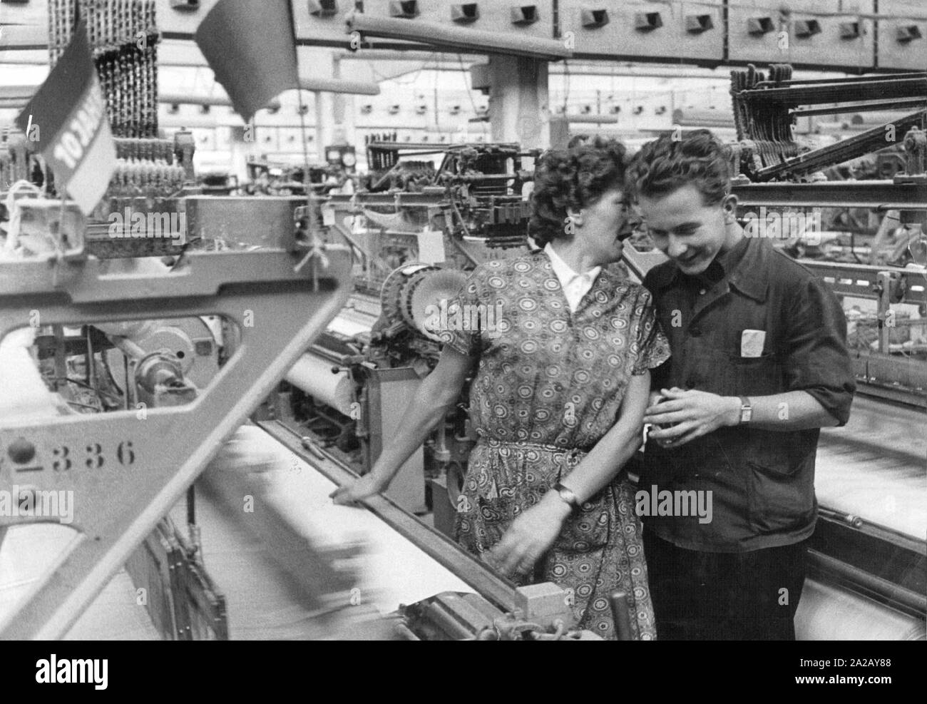 Ein weiblicher und ein männlicher Arbeitnehmer kommunizieren Trotz der Lärm der Maschinen. Auf der Maschine gibt es eine Flagge "10 Jahre DDR". Stockfoto