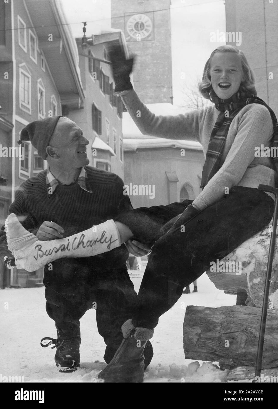 Die 'Rote Teufel' (Red Devil), ein Skilehrer aus Kitzbühel, schreibt 'Bussi Charly' auf dem Bein Gips der Amerikanischen ski Bunny. Undatiertes Bild. Stockfoto