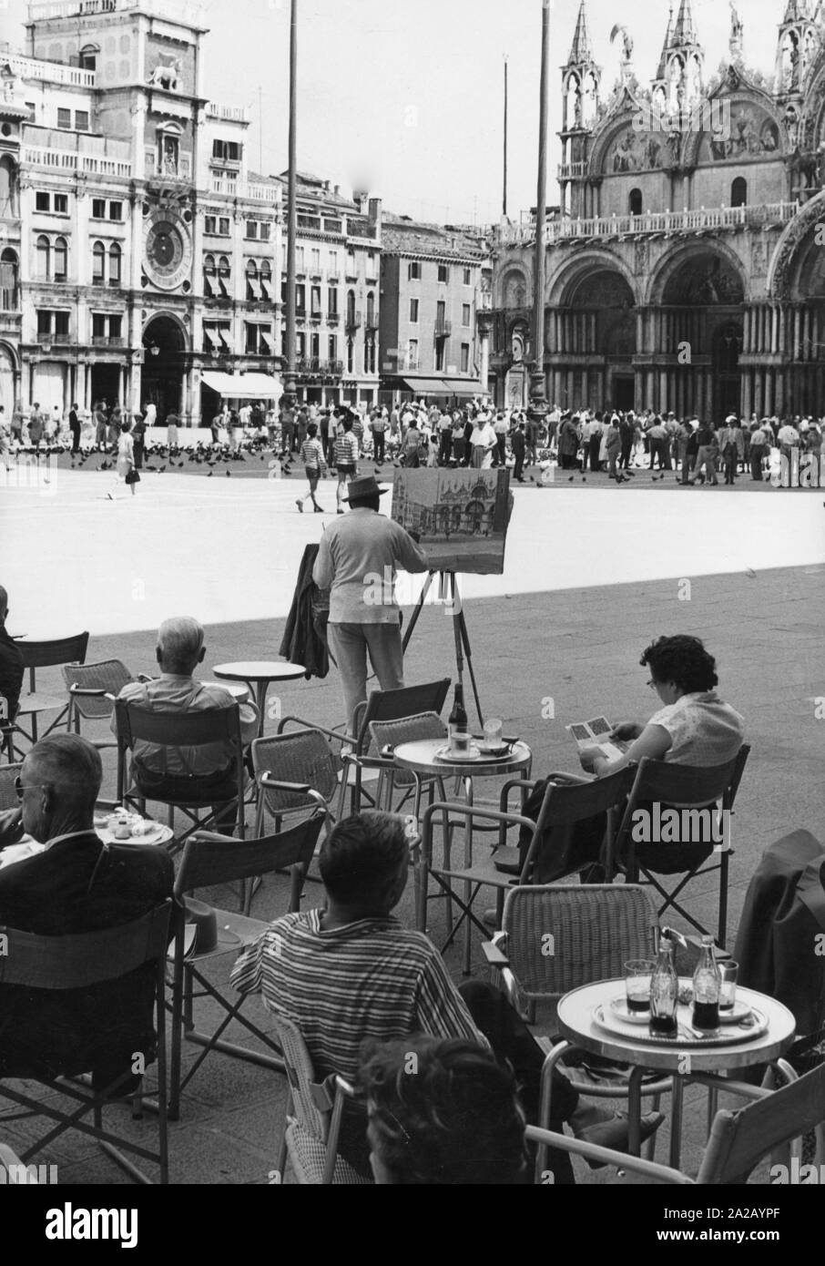 Am Markusplatz in Venedig, links der Hl. Markus Basilika, die Vielzahl von Passanten treiben. Gäste entspannen Sie in einem Cafe, während der Platz selbst und den umliegenden Gebäuden durch unzählige einheimische und exotische Besucher besucht werden. Ein Künstler fängt die Szene in einem Gemälde. Stockfoto