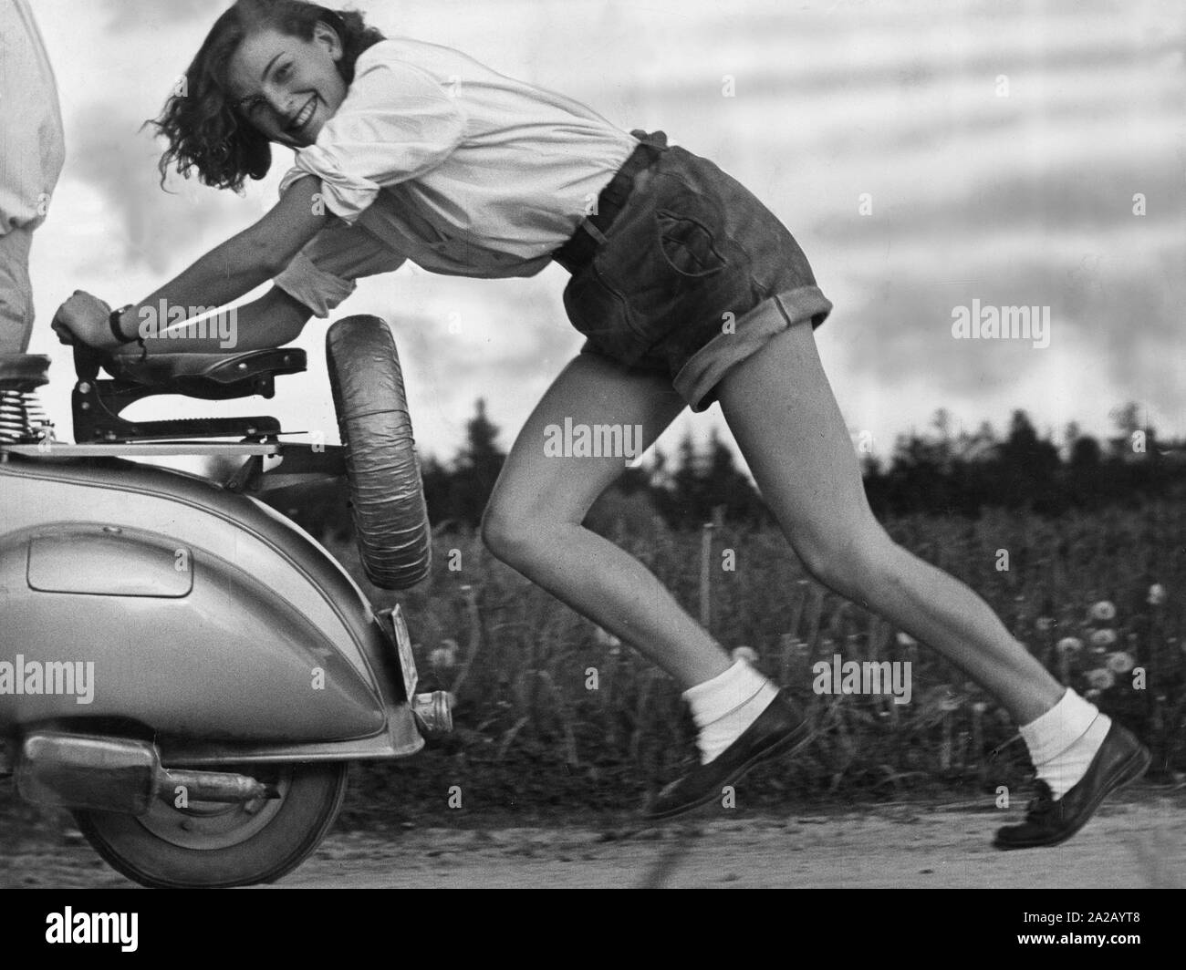 Ein Mädchen in kurzen Lederhosen lacht, während sie einen Roller  Stockfotografie - Alamy