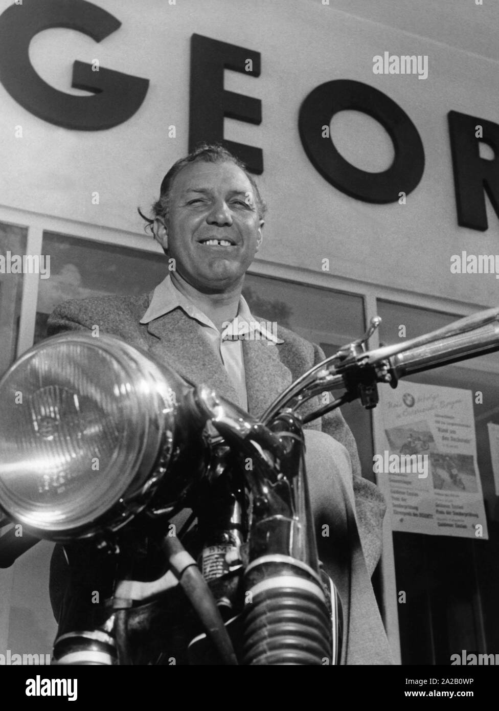 Das Bild zeigt die ehemalige Motorrad Racer Georg Meier (auch genannt: Schorsch Meier). Diese Aufnahme wurde wahrscheinlich nach seiner aktiven Karriere gemacht. Nach seiner Zeit als Rennfahrer Meier übernahm in München die Verteilung und der Verkauf von Motorrädern und Autos von BMW. Im Bild posiert er mit einem BMW Motorrad, wahrscheinlich vor einem seiner Autohäuser. Das Bild ist vermutlich aus den späten 1950er Jahren. Stockfoto