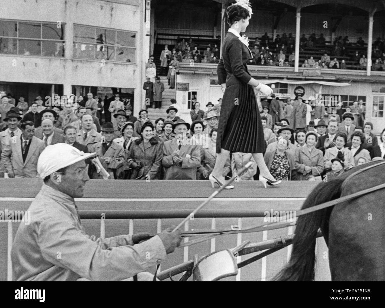 Fashion Show bei einem Pferderennen in München-riem. Ein Modell präsentiert Damenmode zum Publikum, im Vordergrund ein Mann in einem Schlitten Laufwerke Stockfoto