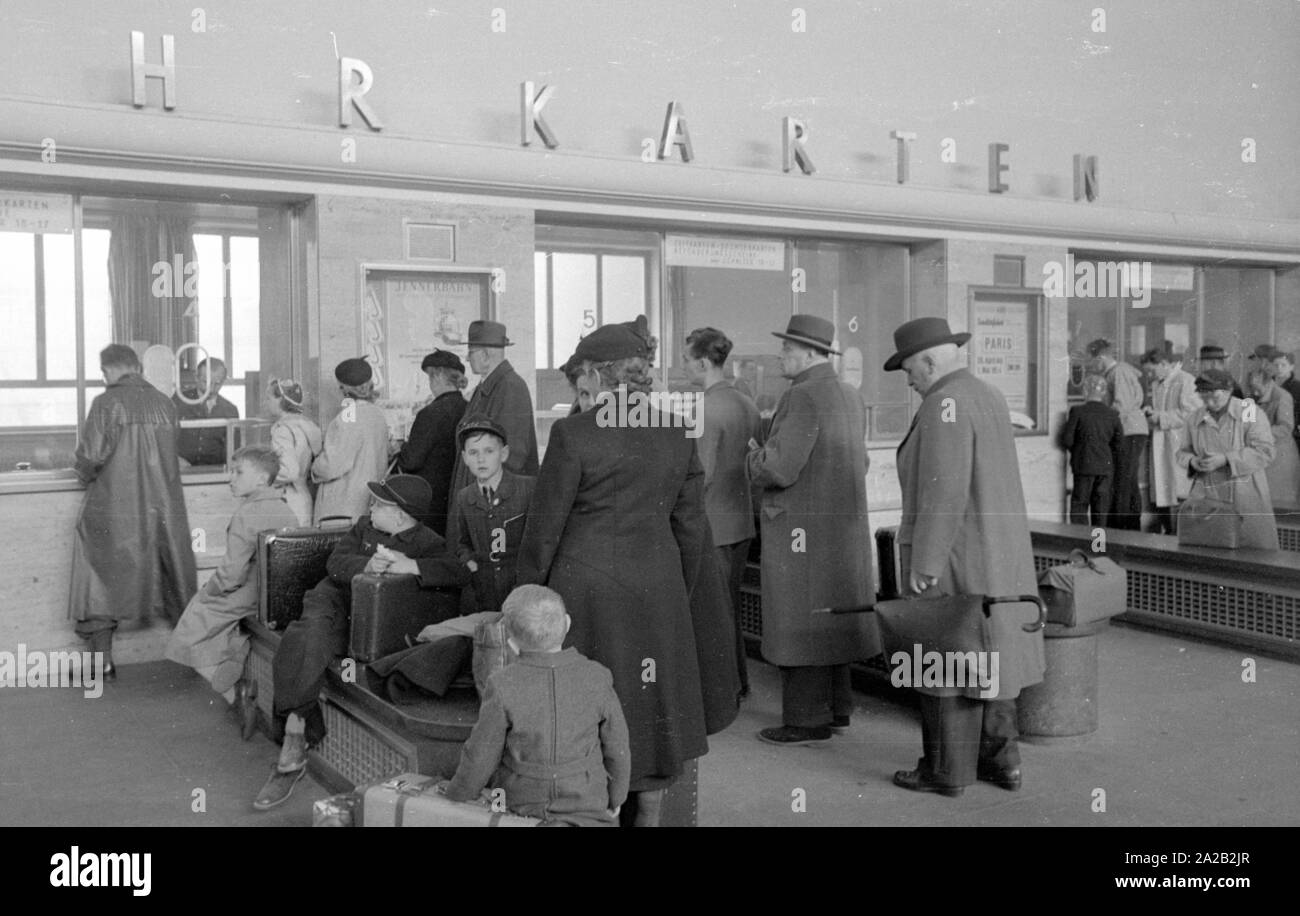 Foto von Passagieren, die an den Kassen warten Tickets in München Hauptbahnhof zu kaufen. Im April 1954, Reisende empfangen Packungsbeilagen für den Mecki Wettbewerb an allen Kassen. Am Wettbewerb kann man Gutscheine für eine Fahrt gewinnen. Stockfoto