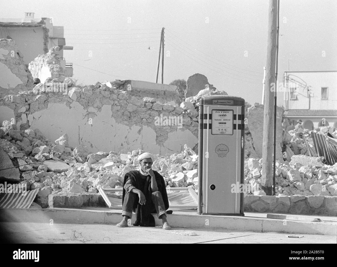 Ein Überlebender des Quake sitzt neben einer Tankstelle. Es gibt Ruinen im Hintergrund. Aus dem Bericht 'Erdbeben in Agadir". Die 1960 Agadir Erdbeben zerstört fast die gesamte Stadt und ist die schwerste Naturkatastrophe in der Geschichte Marokkos angesehen. Stockfoto