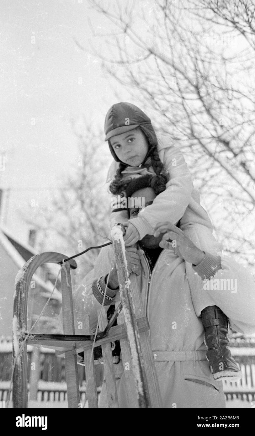 Roberto Blanco spielt im Schnee mit seiner Tochter Mercedes und einem Schlitten im Jahre 1970. Stockfoto