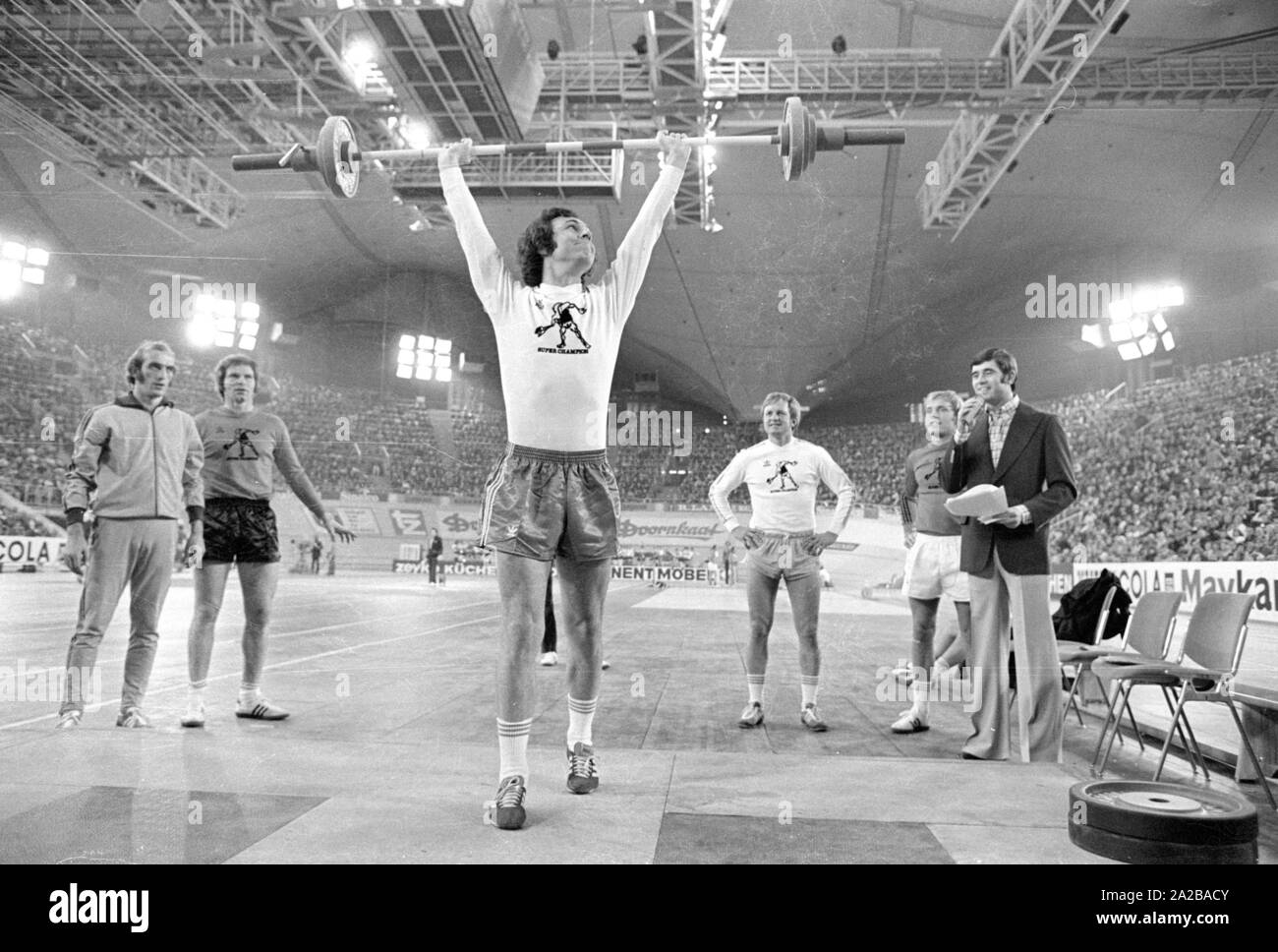Fußballspieler Franz Beckenbauer (Mitte) plantscht im Gewichtheben am Sportpressefest in der Münchner Olympiahalle. Rechts im Bild, der Athlet und Moderator Erhard Keller. Stockfoto