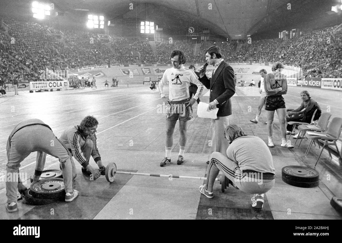 Fußballspieler Franz Beckenbauer plantscht im Gewichtheben am Sportpressefest in der Münchner Olympiahalle. Er hat soeben von Athleten und Moderator Erhard Keller interviewt. Stockfoto