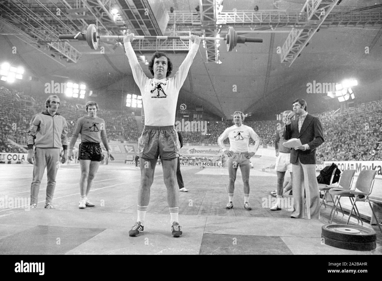 Fußballspieler Franz Beckenbauer plantscht im Gewichtheben am Sportpressefest in der Münchner Olympiahalle. Links im Bild, der Athlet und Moderator Erhard Keller. Stockfoto