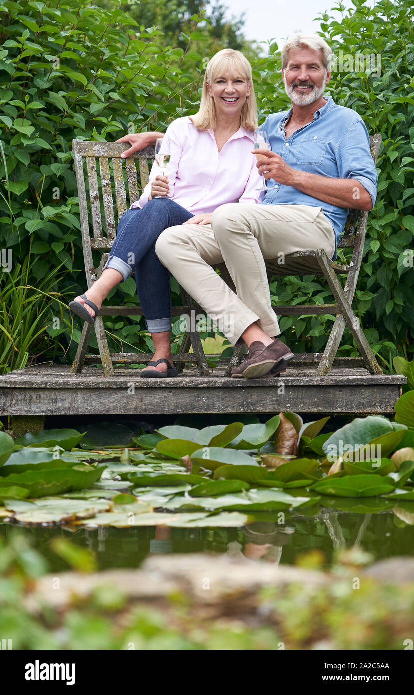Portrait von Reifes Paar feiern mit Champagner Sitzen auf Stühlen auf hölzernen Steg am See Stockfoto Portrait von Reifes Paar feiern mit Champagner Sitzen auf Stühlen auf hölzernen Steg am See Stockfoto