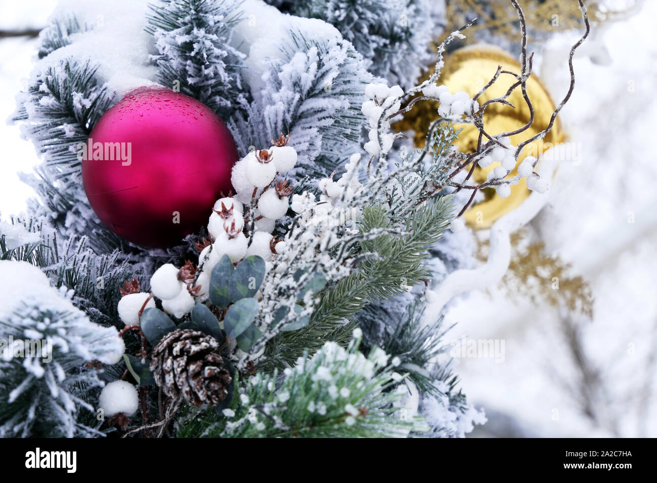 Goldene und rote Weihnachtskugeln mit Kegeln auf tannenzweigen auf Winter Straße. Neues Jahr Dekorationen mit Schnee bedeckt, festliche Ornamente in Stadt Stockfoto