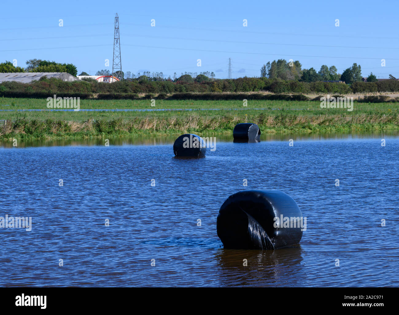 Heuballen in schwarzem Kunststoff teilweise durch Wasser in einem Bauern überschwemmten Feld abgedeckt Stockfoto