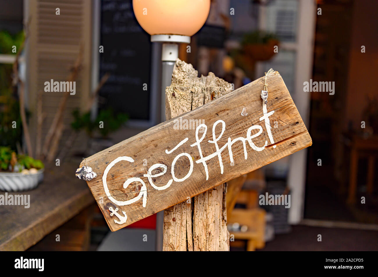Board auf einem hölzernen Pfosten vor einem Geschäft mit dem Wort "geoeffnet" - das ist Deutsch für 'Öffnen'. Stockfoto