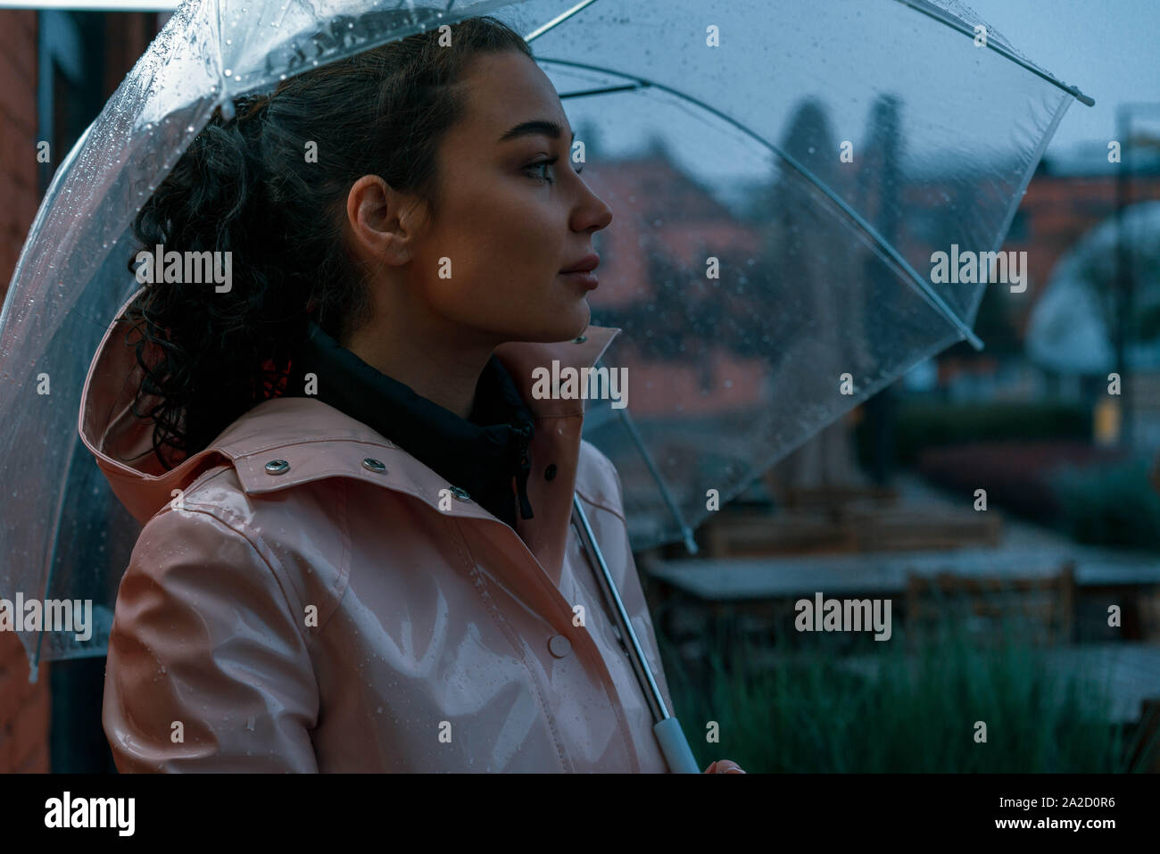 Nachdenklich, hübsches Mädchen Holding transparent Regenschirm während draußen spazieren an regnerischen Herbsttag. Foto sieht aus wie Film oder Film Screenshot. Stockfoto
