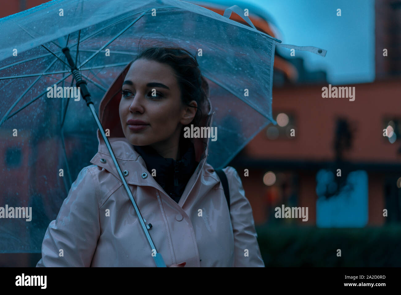 Nachdenklich, hübsches Mädchen Holding transparent Regenschirm während draußen spazieren an regnerischen Herbsttag. Foto sieht aus wie Film oder Film Screenshot. Stockfoto