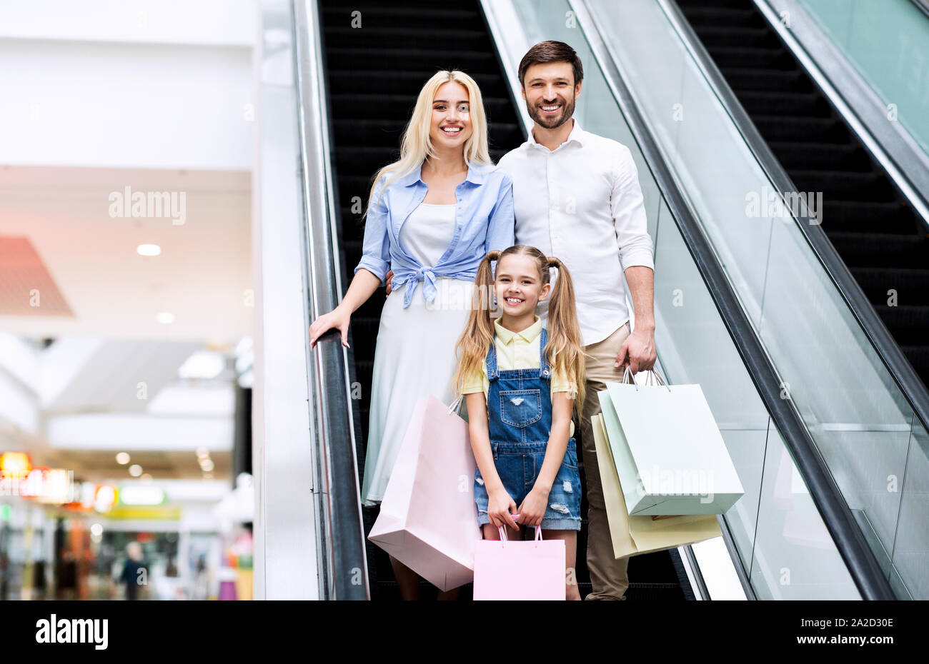 Eltern und Tochter Holding Einkaufstaschen mit Rolltreppe in Mall Stockfoto