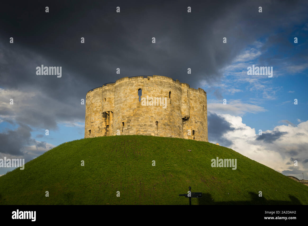 Alten Clifford Tower in der Dämmerung auf einem grünen Hügel und blauer Himmel im Hintergrund mit dunklen Wolken. York in Großbritannien. Stockfoto