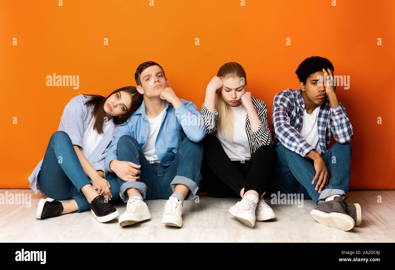 Gelangweilt Klassenkameraden über Orange Studio Hintergrund sitzen Stockfoto