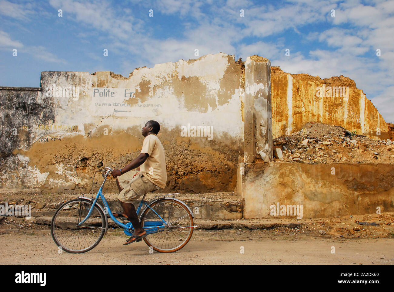 Afrikanische biker Radfahren in eine unbefestigte Straße vor der zerstörten Gebäude Stockfoto